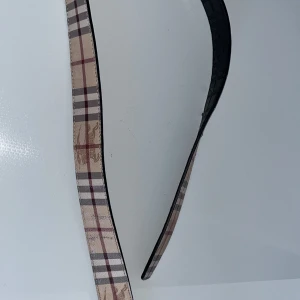 Rutig bälte med spänne burberry - Snyggt bälte med klassiskt rutigt mönster i beige, rött och svart. Bältet har ett stilrent metallspänne som ger en elegant touch. Perfekt för att lyfta vilken outfit som helst.