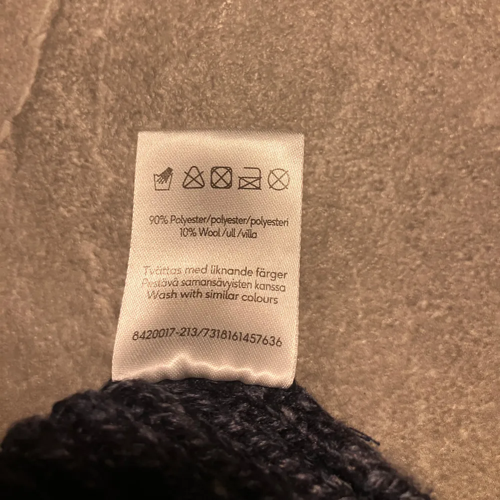 Snygg och varm marinblå mössa, perfekt för kyliga dagar. Tillverkad i en blandning av polyester och ull för extra komfort och värme. Den ribbade designen ger en klassisk look.. Asusteet.