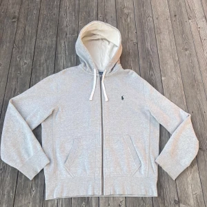 Grå Ralph Lauren Hoodie - Grå Ralph Hoodie i bra skick. Storlek:M. Det finns några skavanker och det är lite nött längst ute på armen samt en liten gulnad på ett ställe i luvan. Men annars i jätte fint skick! Hör av er om frågor!