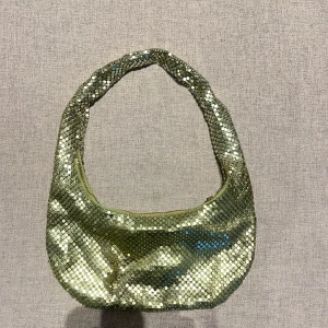 Glittrig axelväska i grön - Snygg glittrig grön axelväska. Väskan har ett grönt innerfoder och en bekväm axelrem. Perfekt för att lägga till lite bling till din outfit.