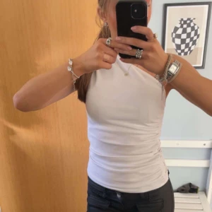 Vit oneshoulder topp från Zara - Säljer en stilren vit oneshoulder topp från Zara. Toppen har en smickrande passform och är perfekt för en trendig look. Den är tillverkad i ett mjukt material som känns skönt mot huden. Perfekt för att lyfta vilken outfit som helst!