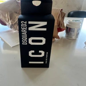 DSQUARED2 Icon Eau de Parfum - Säljer en DSQUARED2 Icon Eau de Parfum i en stilren svart förpackning med vit text. Perfekt för den som vill ha en doft som sticker ut och ger ett starkt intryck. Förpackningen har en modern och minimalistisk design.