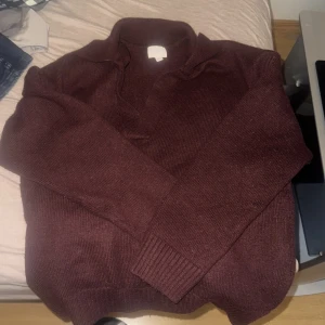 Vinröd stickad tröja - Säljer en mysig vinröd stickad tröja med polokrage. Perfekt för kyliga dagar och ger en stilren look. Tröjan har långa ärmar och ribbade muddar vid ärmslut och nederkant.