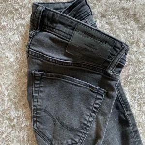 Grå slim jeans från Jack & Jones - Snygga grå slim fit jeans från Jack & Jones, modell Glenn. De har en klassisk femficksdesign och är tillverkade i ett bekvämt denimtyg. Perfekta för en stilren look.