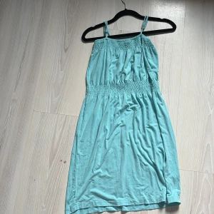 Turkos klänning från W/A - Säljer en söt turkos klänning från W/A med smala axelband och smockdetaljer i midjan. Perfekt för varma dagar. Klänningen har en avslappnad passform och är gjord i ett mjukt material.