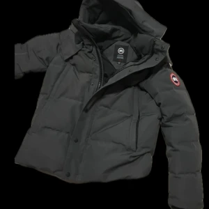Grå dunjacka från Canada Goose - Säljer en stilren grå dunjacka från Canada Goose med huva och dragkedja. Jackan har en klassisk design med långärmade ärmar och en logotyp på armen. Skriv om du har några funderingar eller vill ha fler bilder. NY PRIS ÄR 18000 men dragkedjan är lite sliten och har ej kvar kvittot därav priset(kan gå ner i pris vid snabb affär!!) TAR EMOT BYTEN