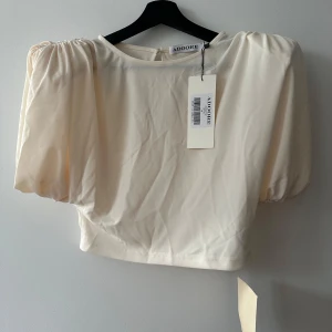 Vit blus från ADOORE - Säljer en stilren vit blus från ADOORE med korta puffärmar och rund halsringning. Perfekt för en elegant look. Blusen är tillverkad i ett mjukt material som ger en skön känsla.