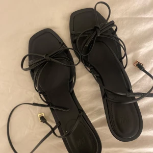 Svarta klackar med klack och snörning - Snygga svarta klackar med låg klack. De har en fyrkantig tå och justerbara remmar med gulddetaljer. Storlek 39, aldrig använda 