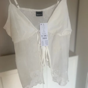 Vitt linne från Gina Tricot - Säljer en elegant vitt linne från Gina Tricot med tunna axelband och vackra broderade blommor. Helt oanvänd med prislapp kvar