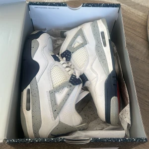 Nike Air Jordans i vit och grå/Jordan 4 midnight navy - Säljer ett par klassiska Nike Air Jordans i vit och grå med snygga detaljer. Skorna har snörning och en ikonisk design med Jumpman-loggan på plösen. Perfekta för sneakerheads som vill ha stil och komfort.