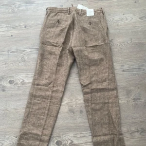 Bruna linnebyxor från Dressmann - Snygga bruna linnebyxor från Dressmann i slim fit. Byxorna har en klassisk design med knappar och dragkedja. Perfekta för en stilren look. Helt nya🙌🏼