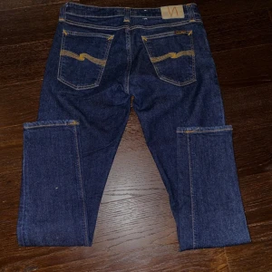 Mörkblå jeans från Nudie Jeans - Snygga mörkblå jeans från Nudie Jeans med klassisk femficksdesign och kontrastsömmar. Jeansen har en rak passform och är tillverkade i slitstarkt denim. Perfekta för en stilren look. Storlek 32/30. Kan gå ner lite i pris