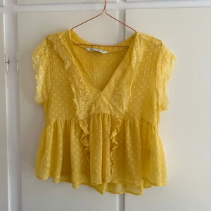 Gul blus med spetsdetaljer - Charmig gul blus från Zara med spetsdetaljer och volanger. Blusen har en v-ringad design och korta ärmar, perfekt för sommarens varma dagar. Den har ett lätt och luftigt material som ger en bekväm passform.