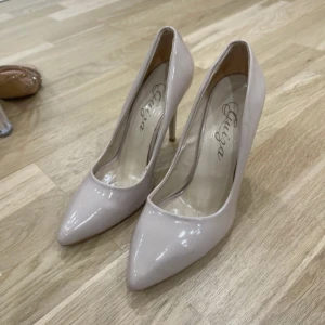 Beige pumps med spetsig tå - Säljer ett par eleganta beige pumps med spetsig tå och hög klack. De är i ett glansigt material som ger en lyxig känsla. Perfekta för fest eller andra speciella tillfällen!