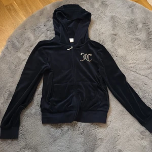 Mörkblå hoodie från Juicy Couture - Junior 9-10 år Säljer en snygg mörkblå hoodie från Juicy Couture med dragkedja och huva. Den har ett glittrigt Juicy Couture-tryck på ryggen och en liten logga på bröstet. Perfekt för en avslappnad stil.