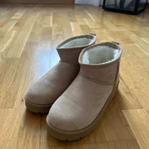 Beige boots med foder - Säljer ett par mysiga beige boots med vitt foder. Perfekta för kalla dagar med sin varma insida och robusta sula. De har en enkel design utan snörning eller dragkedja.