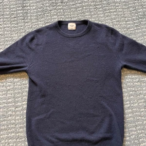 Kashmirtröja från John Henric - Säljer en elegant mörkblå kashmirtröja från John Henric. Tröjan har en klassisk design med rund hals och långa ärmar, perfekt för en stilren look. Tillverkad i 100% kashmir för en lyxig känsla. Passar utmärkt för både vardag och mer uppklädda tillfällen.