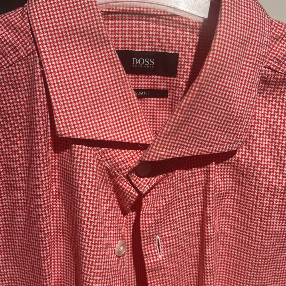 Snygg röd och vit rutig skjorta från Boss i slim fit. Skjortan har långa ärmar och klassisk krage med knappar framtill. Perfekt för en stilren look.. Paidat.