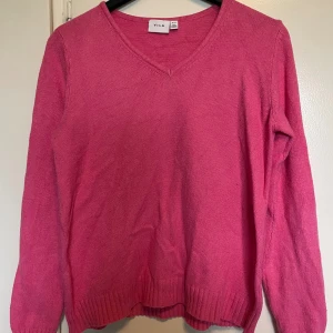 Rosa V-ringad tröja från Vila - Säljer en snygg rosa V-ringad tröja från Vila. Tröjan har långa ärmar och ribbade kanter vid ärmslut och nederkant. Perfekt för en färgglad look!