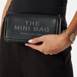 Svart plånbok från Marc Jacobs - Säljer en stilren svart plånbok från Marc Jacobs med texten 'THE MINI BAG' präglad på framsidan. Den är kompakt och perfekt för att bära med sig det viktigaste. En elegant accessoar för alla tillfällen.