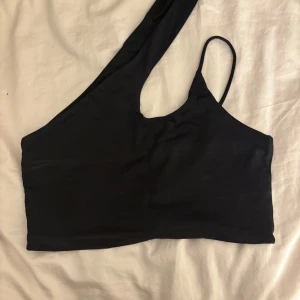 Svart oneshoulder topp från Pull&Bear - Snygg svart oneshoulder topp från Pull&Bear. Perfekt för en trendig look med en unik design som har en axelbandslös sida och en smal axelrem. Tillverkad i ett mjukt och bekvämt material.