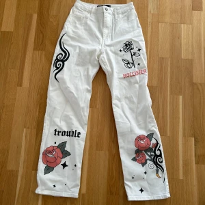 Hollister jeans med tryck - Unika vita jeans från Hollister med coola tryck av rosor, text och mönster. Byxorna har en hög midja och raka ben. Perfekta för dig som vill sticka ut med en edgy look!🤩💞