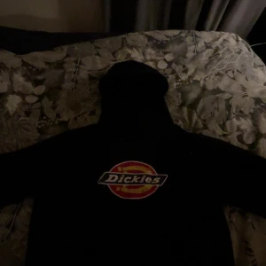 Svart hoodie från Dickies - Säljer en klassisk svart hoodie från Dickies med deras ikoniska logga på bröstet. Perfekt för en avslappnad stil. Hoodien har långa ärmar och en bekväm passform.