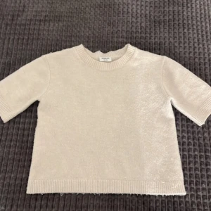 Beige stickad tröja från Kappahl - Säljer en stilren vit tröja från Kappahl. Tröjan har korta ärmar och en rund halsringning med ribbade kanter. Inte använd många gånger och inga fläckar eller hål❣️det noppriga kan jag ta bort❣️❣️