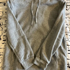 Grå hoodie - Säljer en klassisk grå hoodie med justerbar dragsko i huvan och en stor magficka. Perfekt för en avslappnad stil. Passar bra till både jeans och mjukisbyxor.