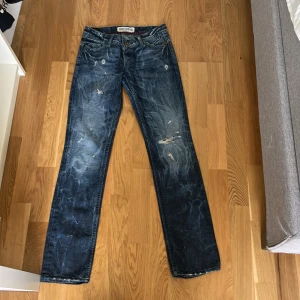 Blå jeans från Tommy Hilfiger - Snygga blå jeans från Tommy Hilfiger med slitna detaljer. Jeansen är köpta secondhand. Märkeslogga på bakfickan ger en extra touch.