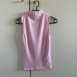 Rosa ärmlös topp - Säljer en söt rosa ärmlös topp med hög krage. Perfekt för varma dagar eller som ett lager under en jacka. Toppen är gjord i ett mjukt och bekvämt material.