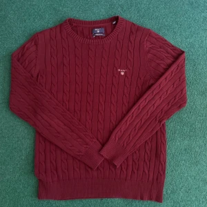 Vinröd stickad tröja från GANT - Säljer en stilren vinröd stickad tröja från GANT med kabelstickat mönster. Tröjan har långa ärmar och en rund halsringning. Perfekt för kyligare dagar. Hör av dig vid intresse! Mycket fint skick, knappt använd. Max 1-2 gånger!