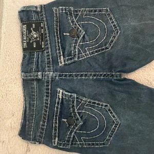 Blå jeans från True Religion - Snygga blå jeans från True Religion med ikoniska bakfickor och kontrastsömmar. De har en klassisk femficksdesign och knappgylf. Perfekta för en avslappnad stil.