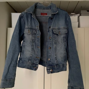 Blå jeansjacka från L.O.G.G. - Säljer en klassisk blå jeansjacka från L.O.G.G. med knappar framtill och två bröstfickor. Jackan en lite mer croppad, tajtare passform och långa ärmar, perfekt för vår och sommar. En tidlös favorit i garderoben! 💙