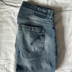 Dondup George Jeans Blå - Snygga blå Dondup George jeans i storlek 33 men passar 31-32. Jeansen har slitningar på knä och lår. Klassisk femficksmodell med broderade detaljer på bakfickorna och logga baktill i midjan. Jeansen har en smal passform och är tillverkade i stretchig denim för extra komfort.