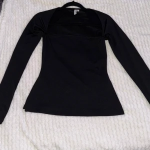 Svart långärmad topp från Nelly - Säljer en skitsnygg svart långärmad topp från Nelly i storlek S. Modellen är figurnära med lätt utsvängd nederdel och sydda detaljer vid axlarna. Materialet är stretchigt. Har slits vid både höger och vänster nederdel. Skriv för fler bilder 