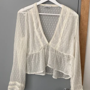 Vit transparent blus med spetsdetaljer - Romantisk vit blus från Stradivarius i transparent tyg med diskret prickigt mönster. Djup v-ringning, spetskantade detaljer och volang nedtill. Långärmad och luftig, perfekt för lager-på-lager eller till ett par jeans.Perfekta toppen för sommaren💘💞💕🩷Strilek L men passar den som brukar ha S/36-38