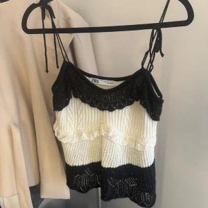 Stickad linnetopp från Zara i svart och vitt - Supersöt stickad linnetopp från Zara med smala axelband som knyts. Toppen är svart och vit med virkade detaljer, volang och mönstrad struktur. Perfekt för dig som gillar en unik och trendig look med lite retrovibbar.
