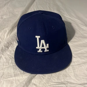 LA Dodgers blå keps 59FIFTY 7 1/8 - Snygg blå LA Dodgers keps från New Era 59FIFTY-serien med broderad LA-logga framtill och 1980 All-Star Game patch på sidan. Klassisk rak skärm och cool basebollstil. Perfekt för dig som gillar sport och streetwear.