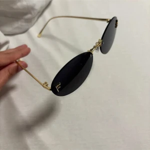 Fendi- Svarta ovala solglasögon - Snygga solglasögon med svarta ovala glas och tunna guldfärgade bågar. Minimalistisk design som ger en clean och modern vibe. Perfekta för att lyfta din stil till nästa nivå.