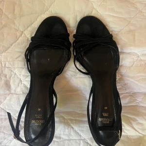 Svarta mockasandaler med klack från Zara - Svarta sandaler från Zara med smala remmar och öppen tå. Skorna har en elegant låg klack och är gjorda i mjuk mocka. Perfekta för dig som gillar stilrena och minimalistiska skor med en feminin touch.