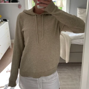 stickad hoodie - Mysig beige stickad hoodie med huva och snörning. Tröjan har lång ärm, ribbade muddar och en avslappnad passform. Den är i fint skick! Hör av dig vid frågor💞