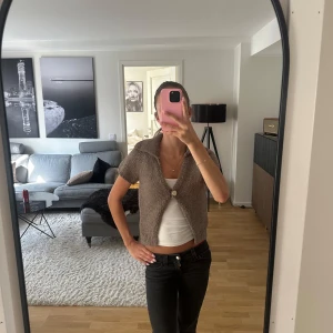 Brun stickad väst från Zara - Kortärmad stickad väst från Zara i en snygg brun nyans. Västen har en bred krage, en enkel knapp framtill och ribbade kanter. Perfekt att slänga över en topp för en chill och trendig look. Endast använd ett fåtal gånger och säljer då den inte kommer till användning!