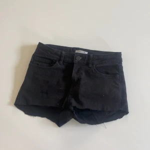 Svarta jeansshorts - Svarta jeansshorts från Lindex med råa kanter och klassisk femficksdesign. De har normal passform och low waist , perfekt för en avslappnad stil. Materialet är jeans och färgen är helsvart, vilket gör dem enkla att matcha med allt.