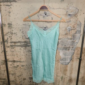 Mintgrön spetsklänning med smala axelband - Söt mintgrön kortklänning med tunna axelband och v-ringning. Klänningen har fina spetsdetaljer vid halsringning och nederkant, och är gjord i ett glansigt, silkesliknande material. Perfekt för sommarens varma dagar.