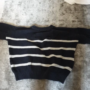 Randig stickad tröja från 157 - Mysig svart stickad tröja från 157 med vita horisontella ränder. Tröjan har ribbad hals, ärmslut och nederkant samt lång ärm. Perfekt för dig som gillar klassisk stil med en twist. Snygg till både jeans och kjol!