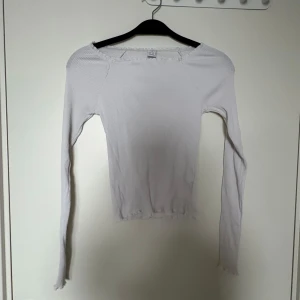 Vit ribbad långärmad topp Lindex - Vit långärmad topp från Lindex med ribbad struktur och stretchigt material. Modellen har smala ärmar, lätt volangkant vid halsringning och nederkant samt en slim passform. Perfekt att styla med jeans eller kjol för en clean look.