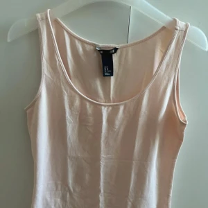 Ljusrosa linnetopp från H&M - Enkel och stilren ljusrosa linnetopp från H&M med rund halsringning och ärmlös design. Perfekt att matcha med jeans eller kjol för en avslappnad look