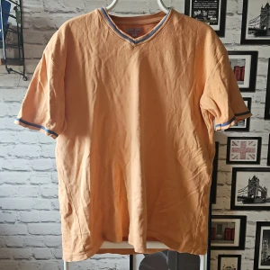 Persikofärgad t-shirt från Batistini - Snygg persikofärgad t-shirt från Batistini i storlek XL. T-shirten har korta ärmar och v-ringad hals med blå detaljer vid halsringning och ärmslut. Perfekt för dig som gillar en chill och stilren look.