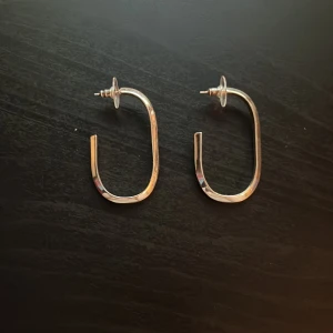 Silvriga chunky örhängen i oval form - Säljer ett par silvriga chunky örhängen med modern, oval och öppen design. De är blanka och har en cool, minimalistisk vibe som passar perfekt till en trendig look. Perfekta för dig som gillar statement-smycken med stilren känsla. Köpt från H&M men aldrig använt.